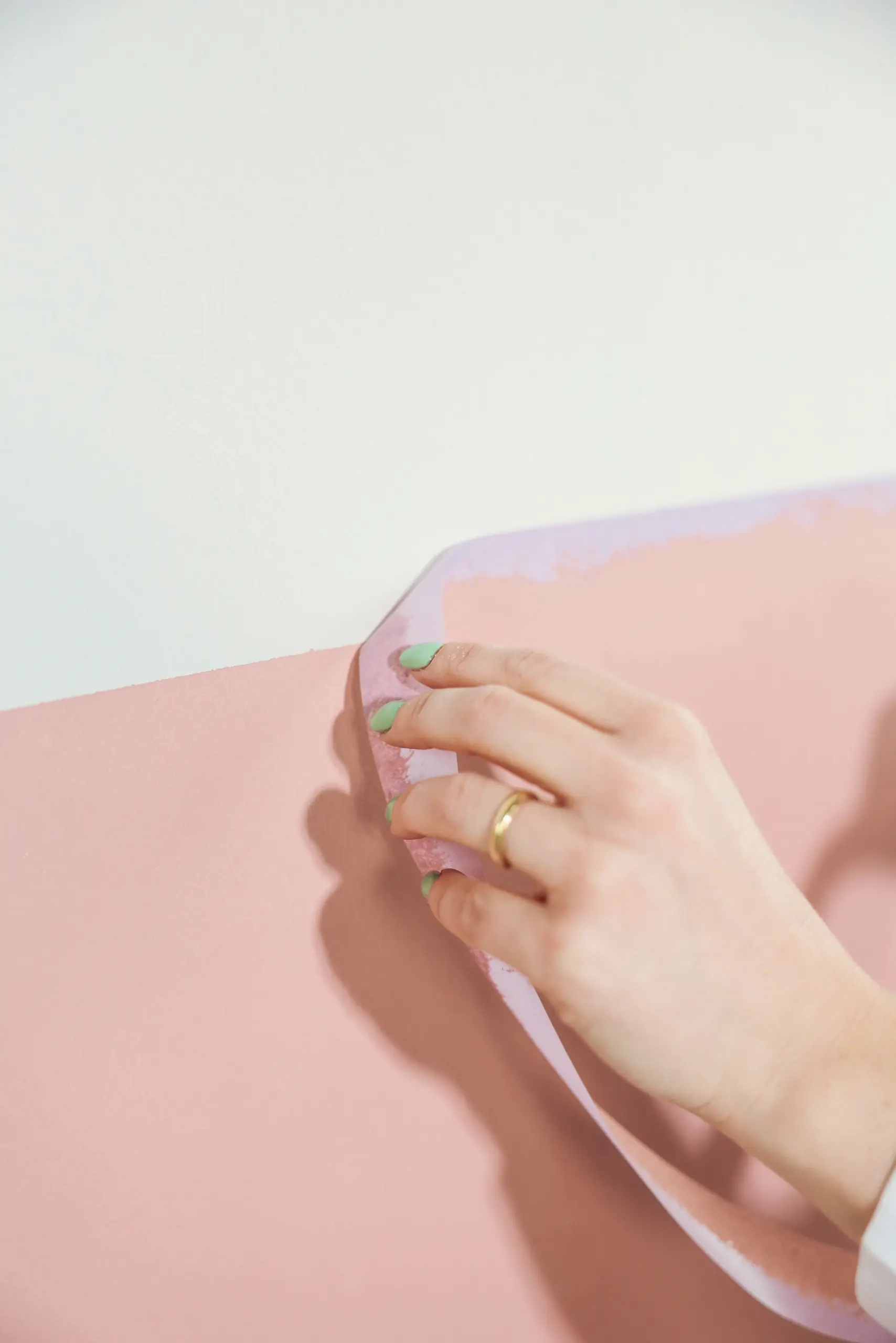 Kleurstaal van Roll met een roze tint, vastgehouden door een hand met groene nagels en gouden ring, tegen een witte achtergrond.